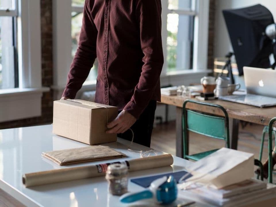 Una persona que prepara un pedido en una caja de cartón sobre la mesa de un estudio